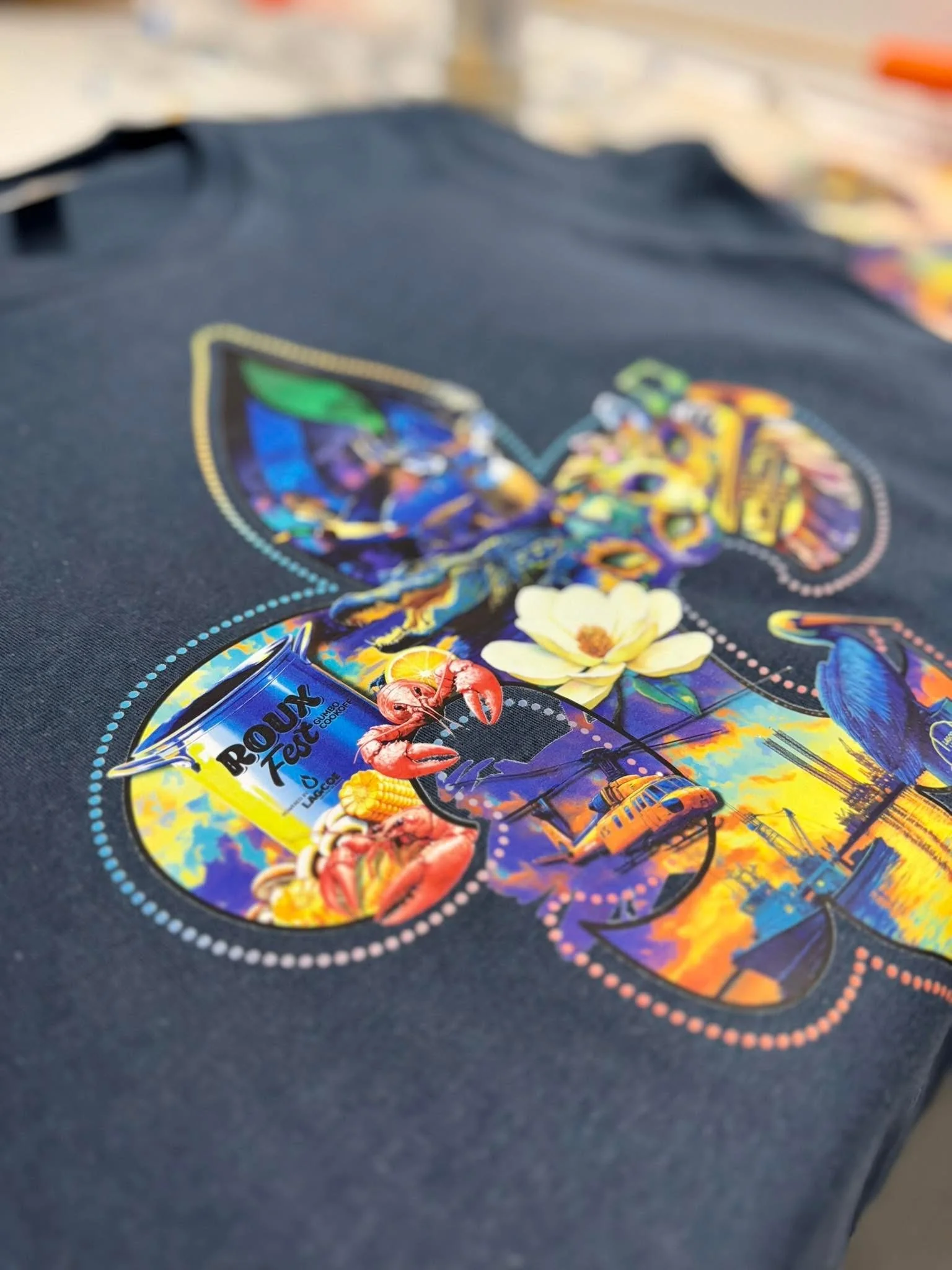 Dark navy t-shirt featuring a colorful screen-printed design for Roux Fest with crawfish, flowers, and Louisiana imagery