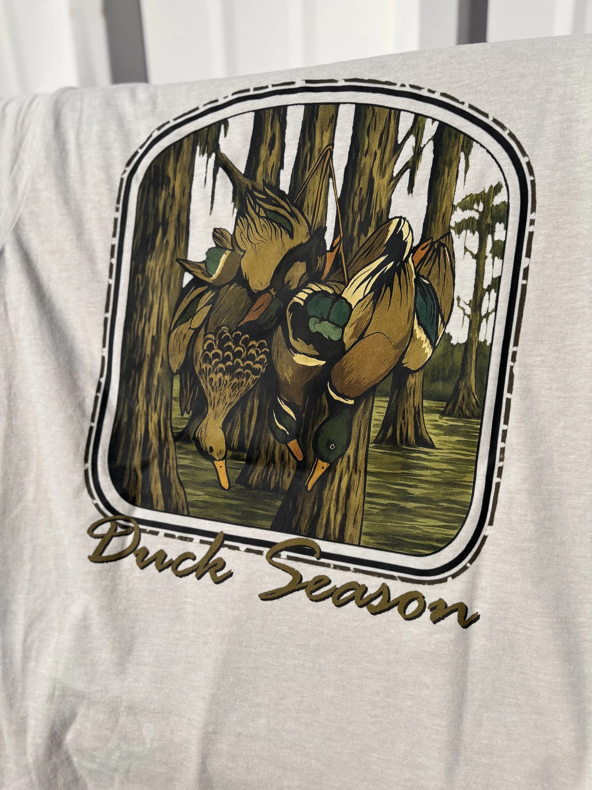 Light grey t-shirt featuring a full-front DTF graphic of hanging ducks in a swampy forest scene with the text Duck Season