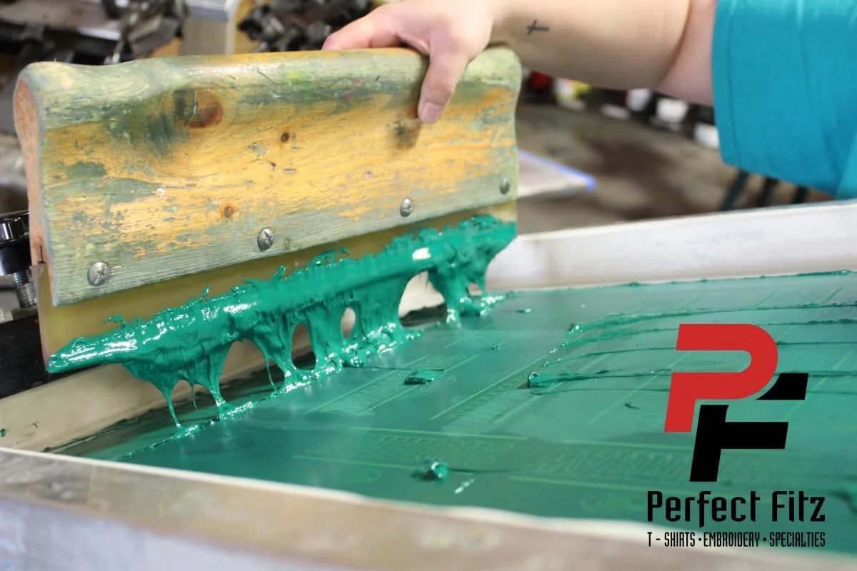 Green ink being squeegeed across a screen printing mesh at Perfect Fitz